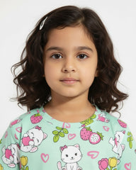 Young girl wearing a light green shirt with cartoon cat designs on a white background