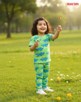Child in a green and blue nightwear outfit standing in a grassy field with a butterfly.