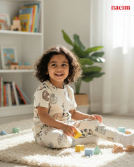 Child wear pajama set playing with toys on a carpeted floor in a room with books and plants.