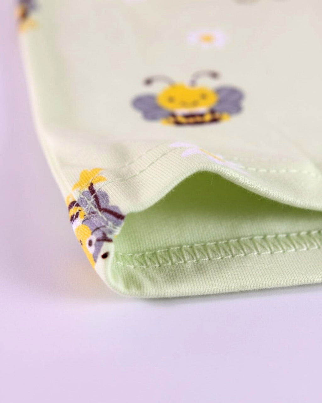 Folded green fabric for pajama with bee pattern on a light purple background
