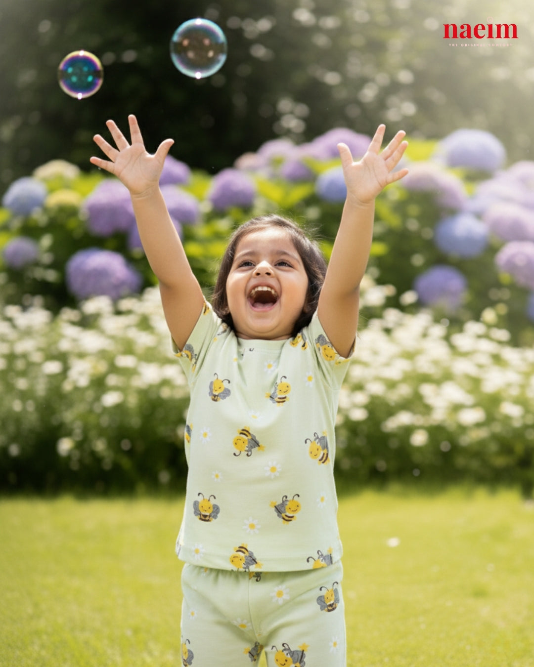 Child in pajama playing with bubbles in a garden with flowers and grass.