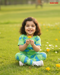 Child wear green pajama set sitting on grass holding a flower, with 'naeim' logo in the corner