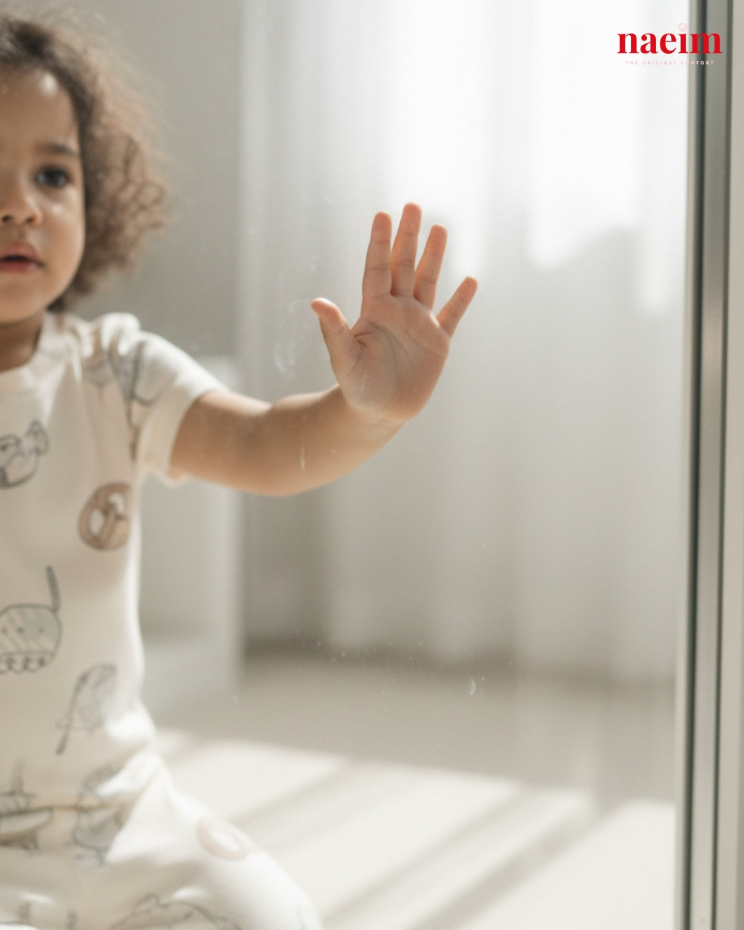 Child in food themed pajama set reaching out towards a glass door with 'naeim' branding.
