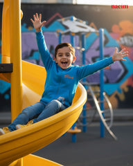 Child in a blue sweatshirt sliding down a yellow slide at a playground with colorful graffiti in the background.