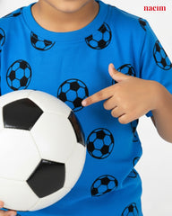 Child wearing a blue shirt with soccer ball patterns, holding a soccer ball and pointing at it.