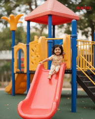 Child sliding down a red slide at a playground with colorful equipment.