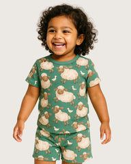 Child wearing a green pajama set with sheep pattern on a plain background