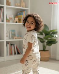 Child wearing pajamas with a pattern in a room with a bookshelf and plant.